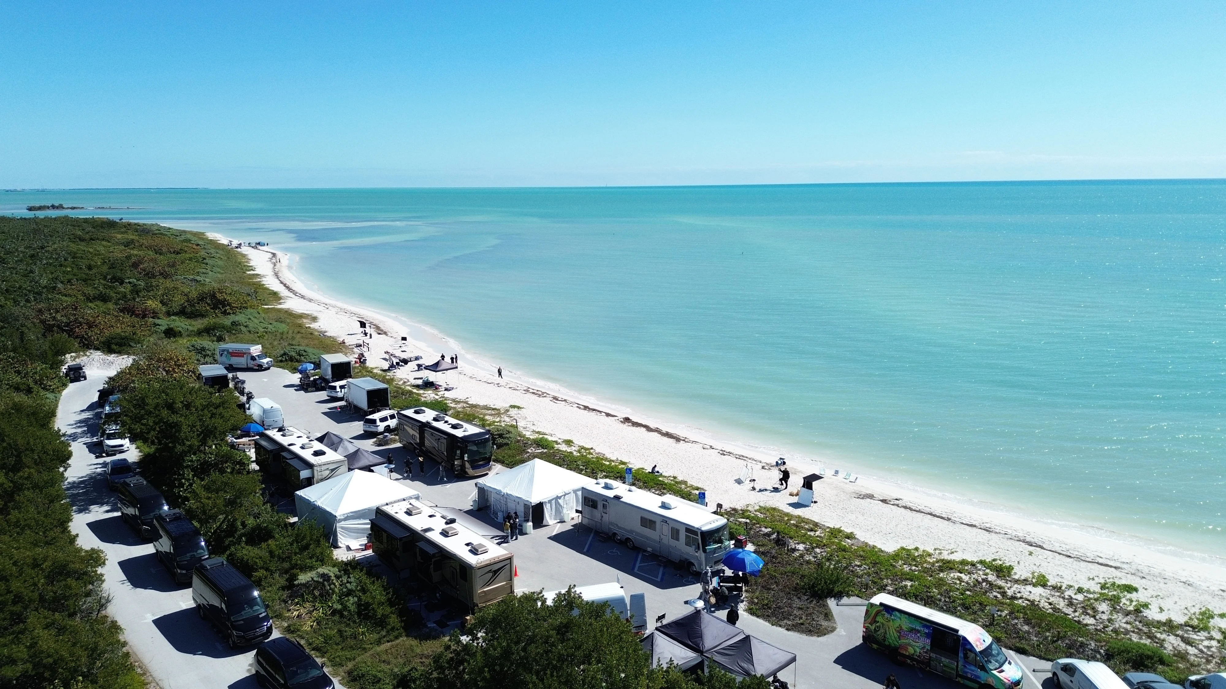 Aerial view of beach production setup with tents and vehicles